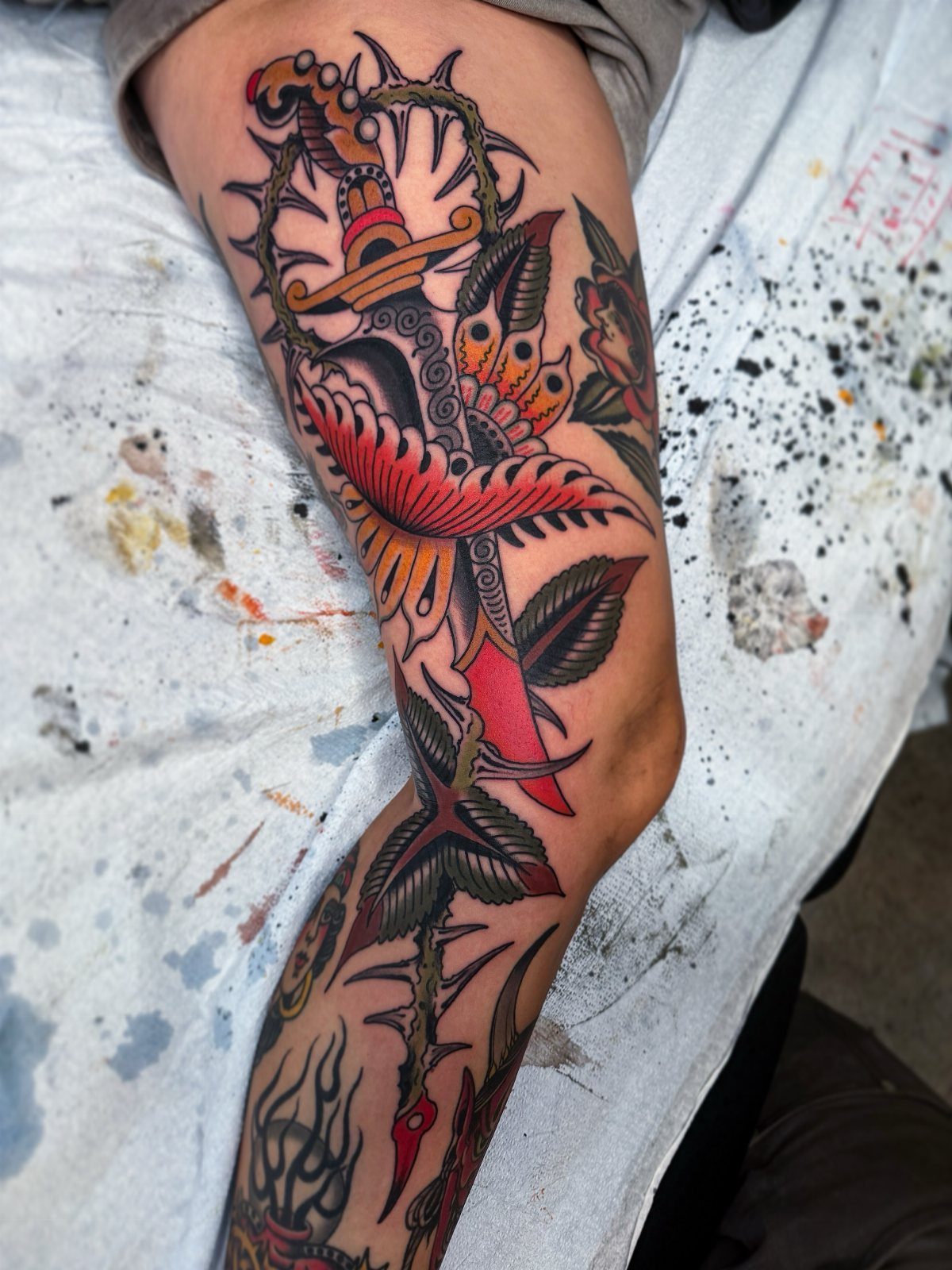 A large American traditional dagger tattoo with thorns and leaves on a person's leg.