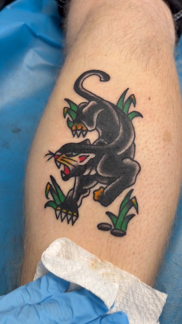 A black panther tattoo with green leaves on a person's leg.