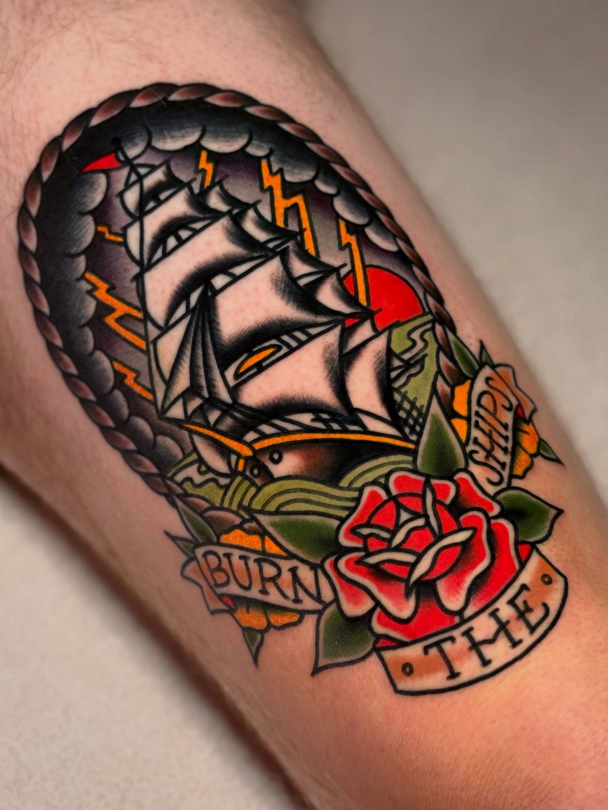A colorful American traditional tattoo of a sailing ship and a red rose on skin.