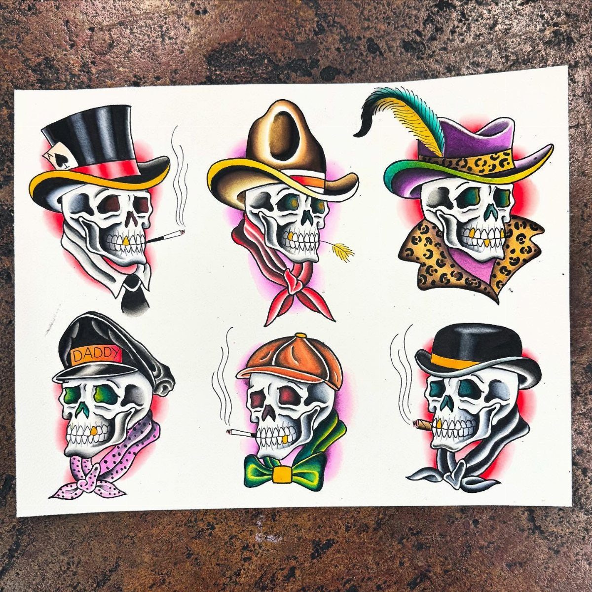 Six stylized skull tattoo designs wearing various colorful hats and accessories on white paper.