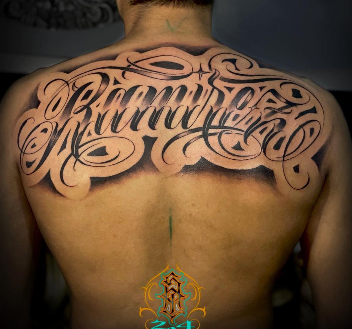 7 Back Tattoo Writing Ideas for Lettering That Lasts 1 Large black ink tattoo with stylized cursive lettering and decorative swirls on a person's upper back.