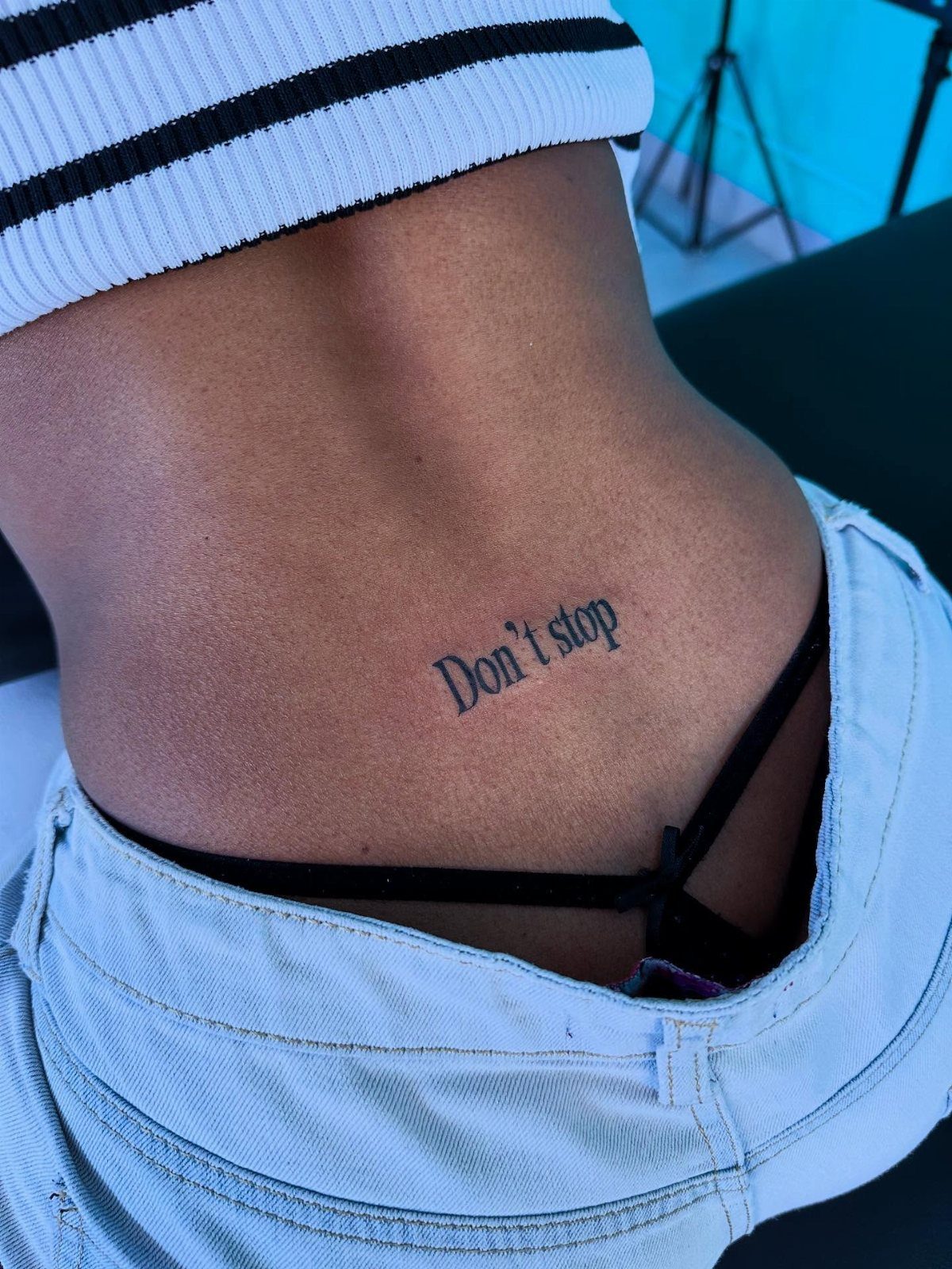 7 Back Tattoo Writing Ideas for Lettering That Lasts 6 A small black ink tattoo reading Don't stop on a person's lower back.