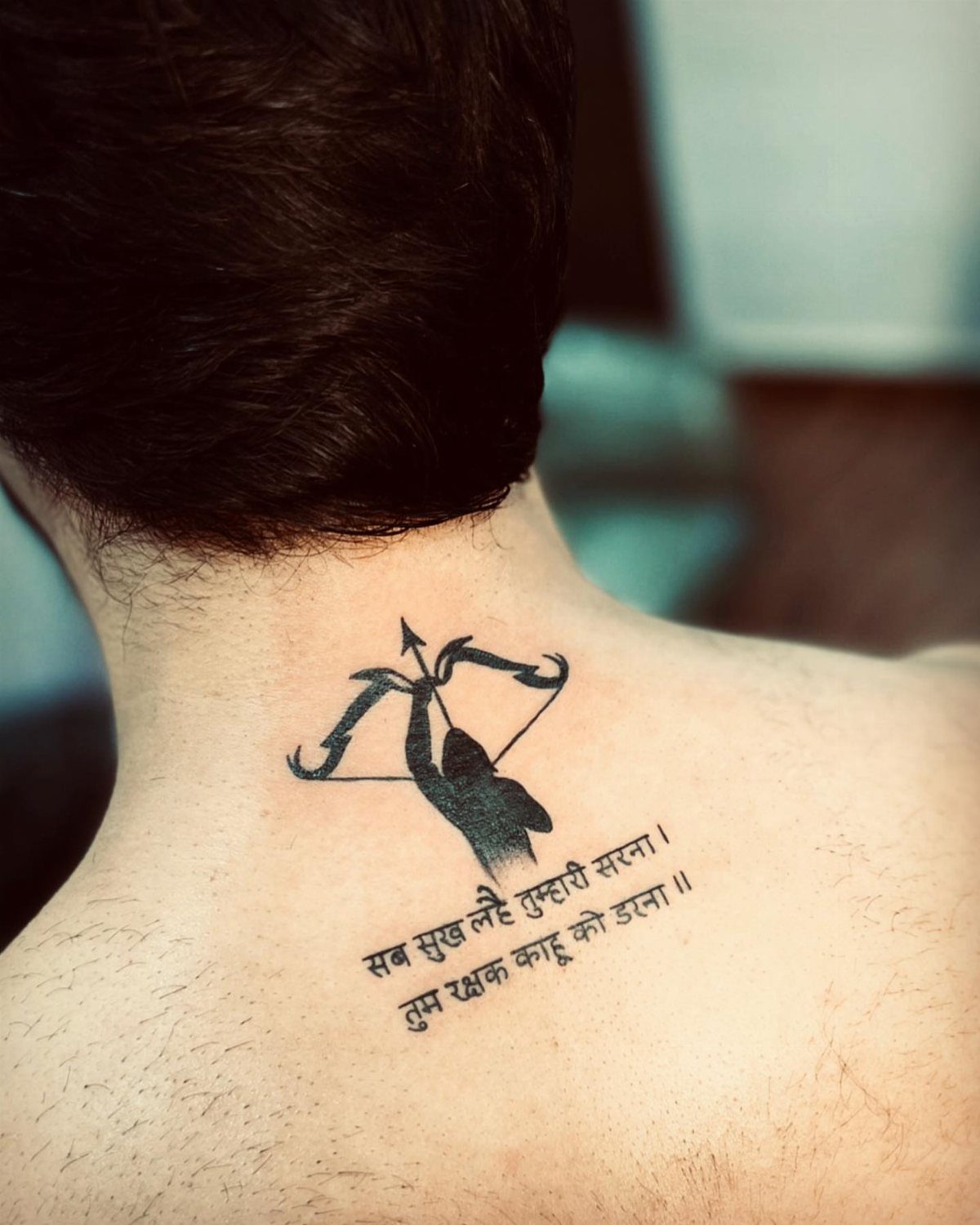 7 Back Tattoo Writing Ideas for Lettering That Lasts 7 A black ink tattoo of a bow and arrow with Hindi text on a person's upper back.