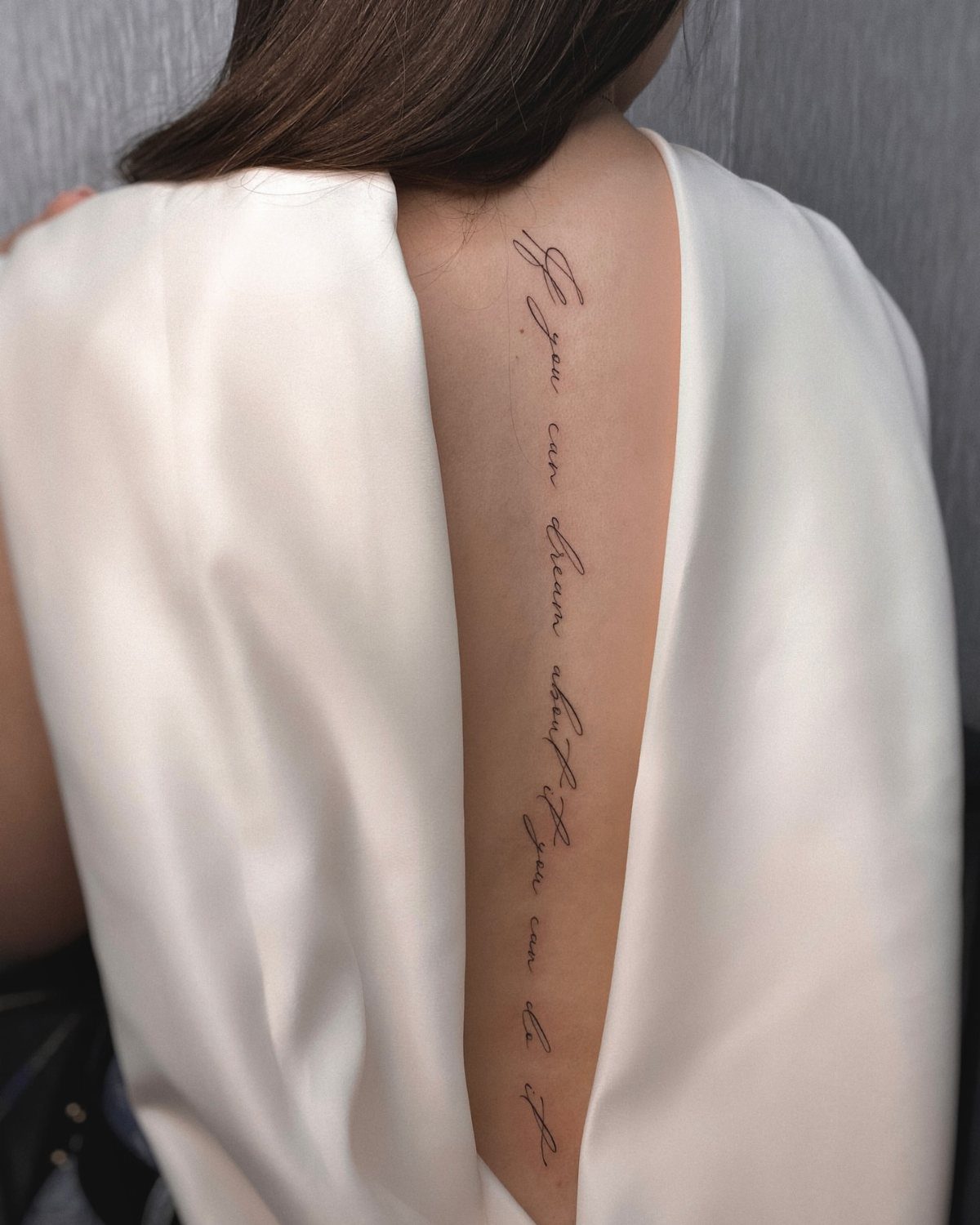 7 Back Tattoo Writing Ideas for Lettering That Lasts 2 A vertical cursive script tattoo running down the center of a person's bare back.