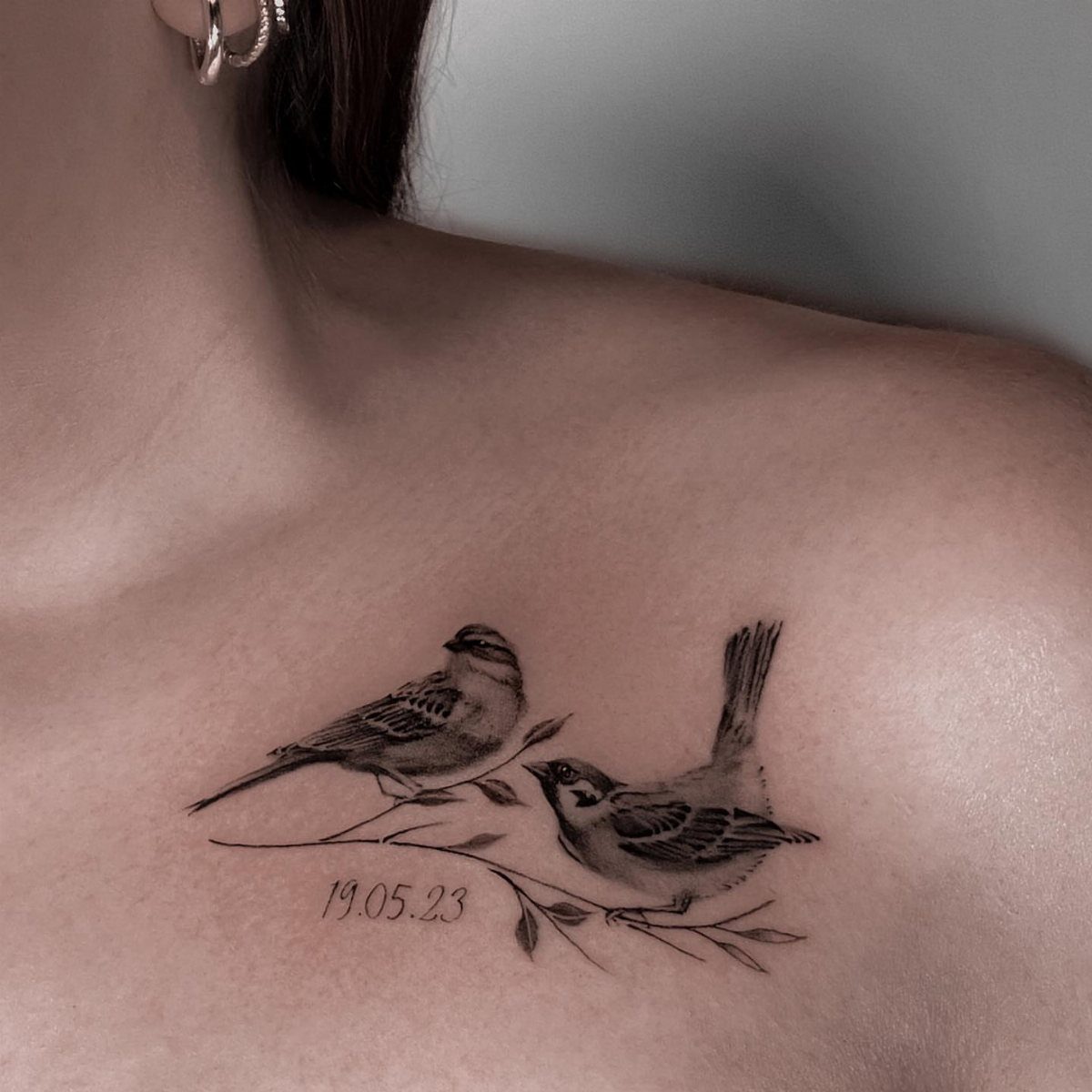 Two small birds perched on a delicate branch tattooed on a person's collarbone.