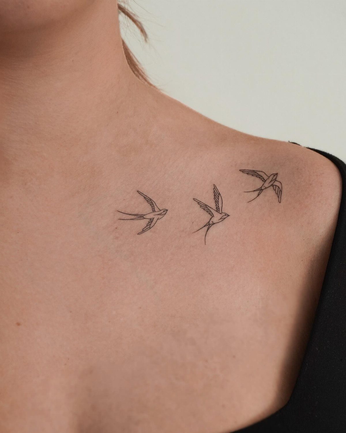 Three small fine line bird tattoos flying along a person's collarbone.