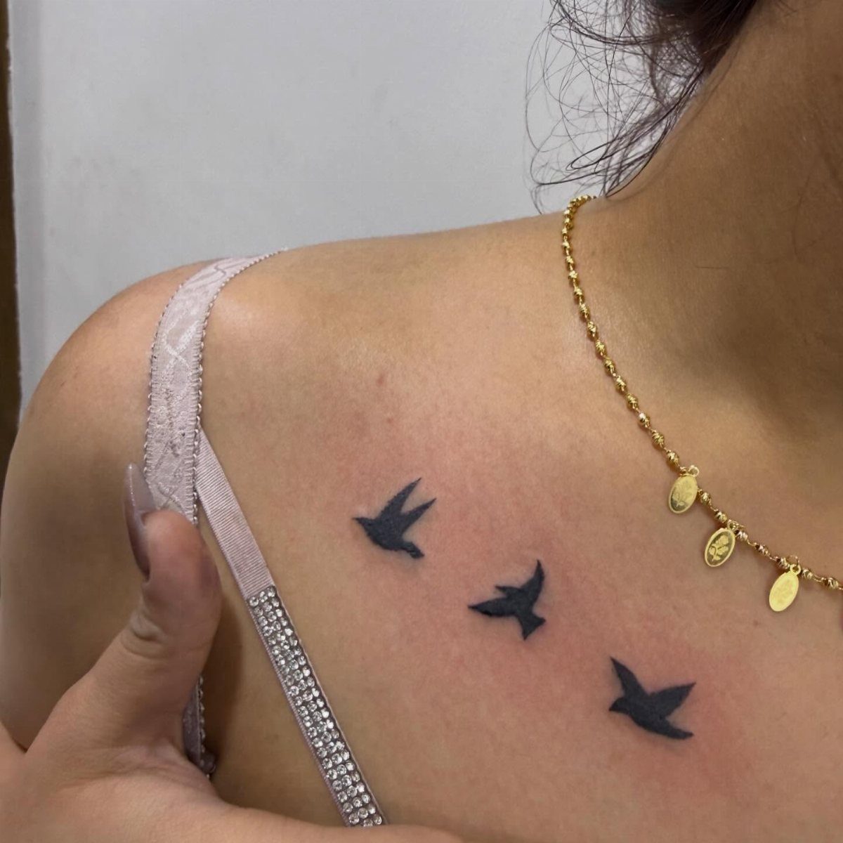 Three small black silhouette bird tattoos flying along a person's collarbone area.