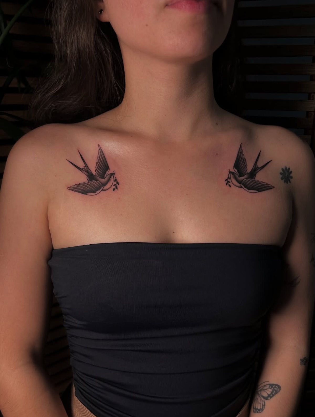 Two traditional style swallow tattoos positioned symmetrically on a person's collarbones.