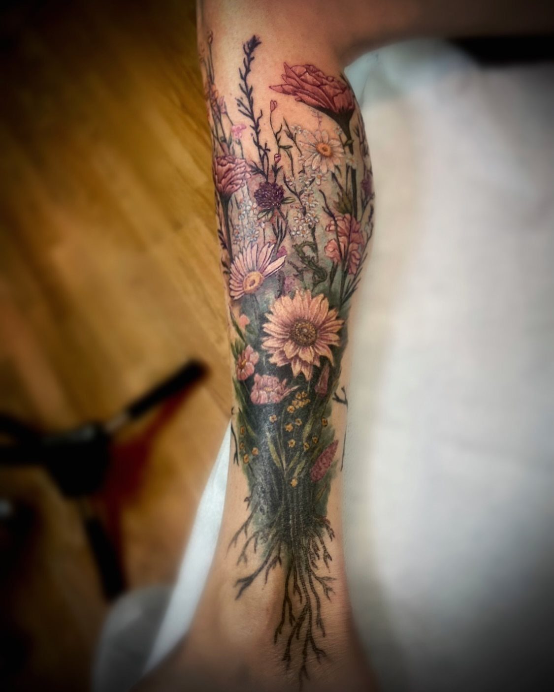 A colorful wildflower tattoo with pink and white blossoms covering a person's forearm.
