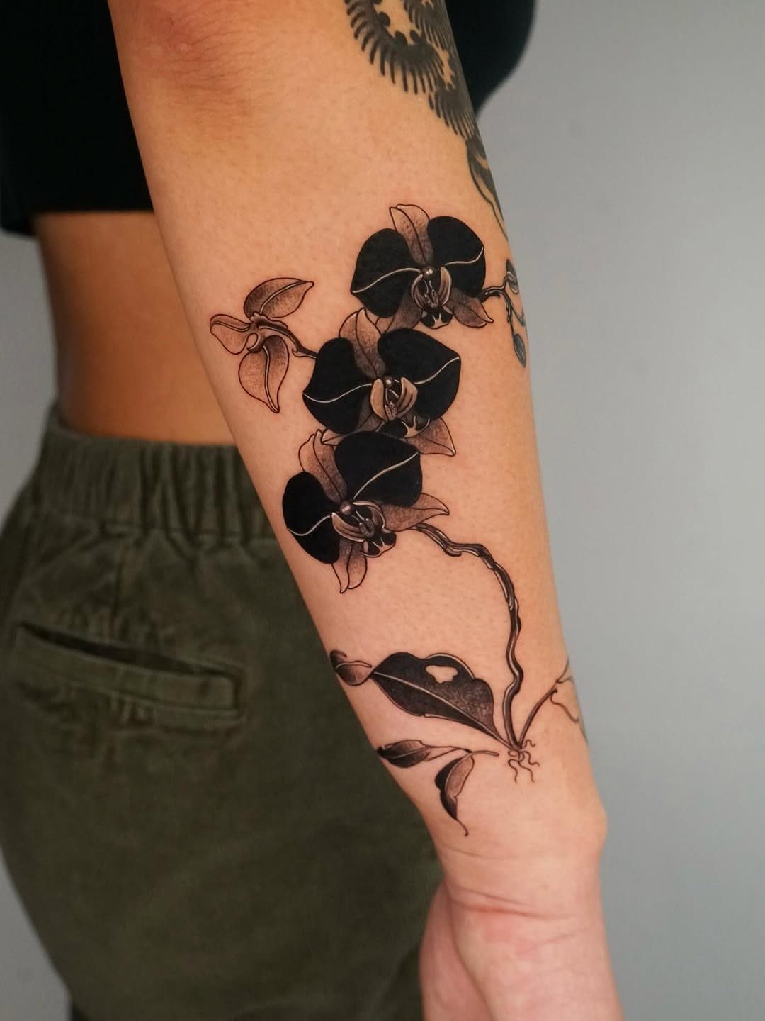 Black ink orchid tattoo with dark shading on a person's forearm.