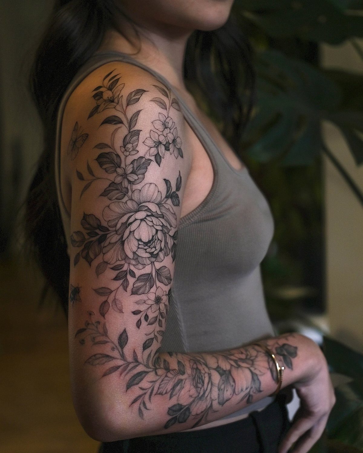 A woman displaying a large black ink floral sleeve tattoo covering her entire arm.