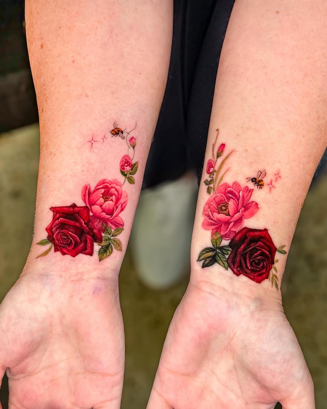 Two forearms displaying vibrant red rose and pink peony botanical tattoos with green leaves.