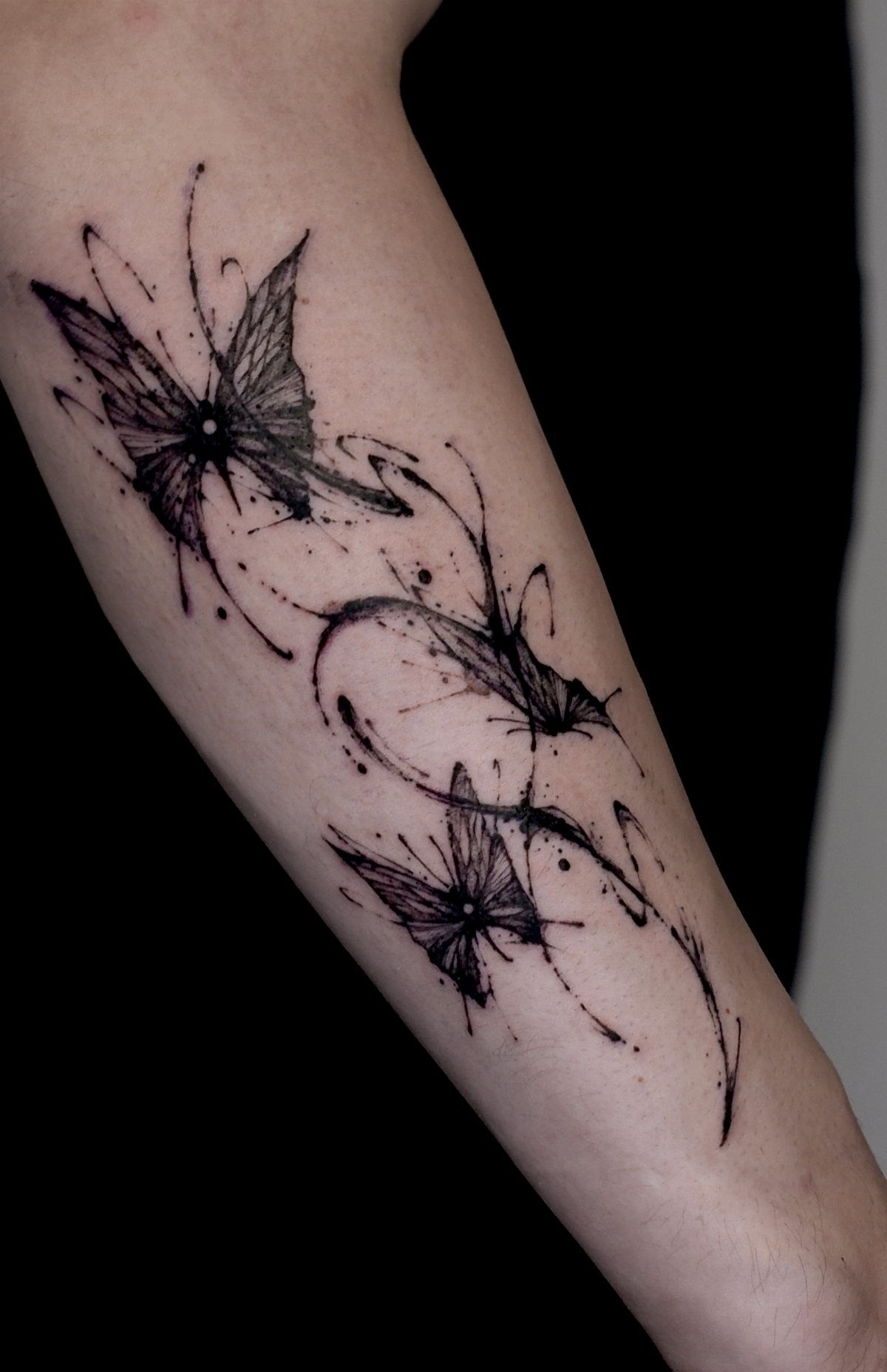 Three black ink butterfly tattoos with stylized wispy lines on a person's forearm.