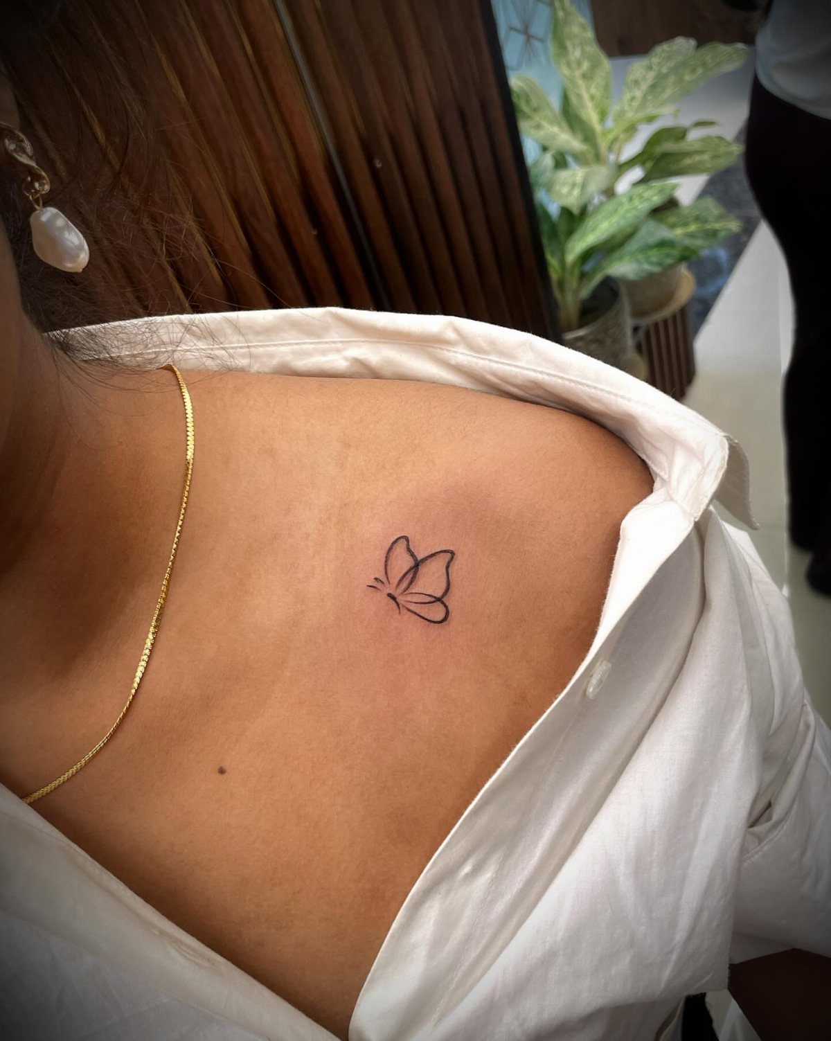 A small, simple black ink butterfly outline tattoo on a person's shoulder.