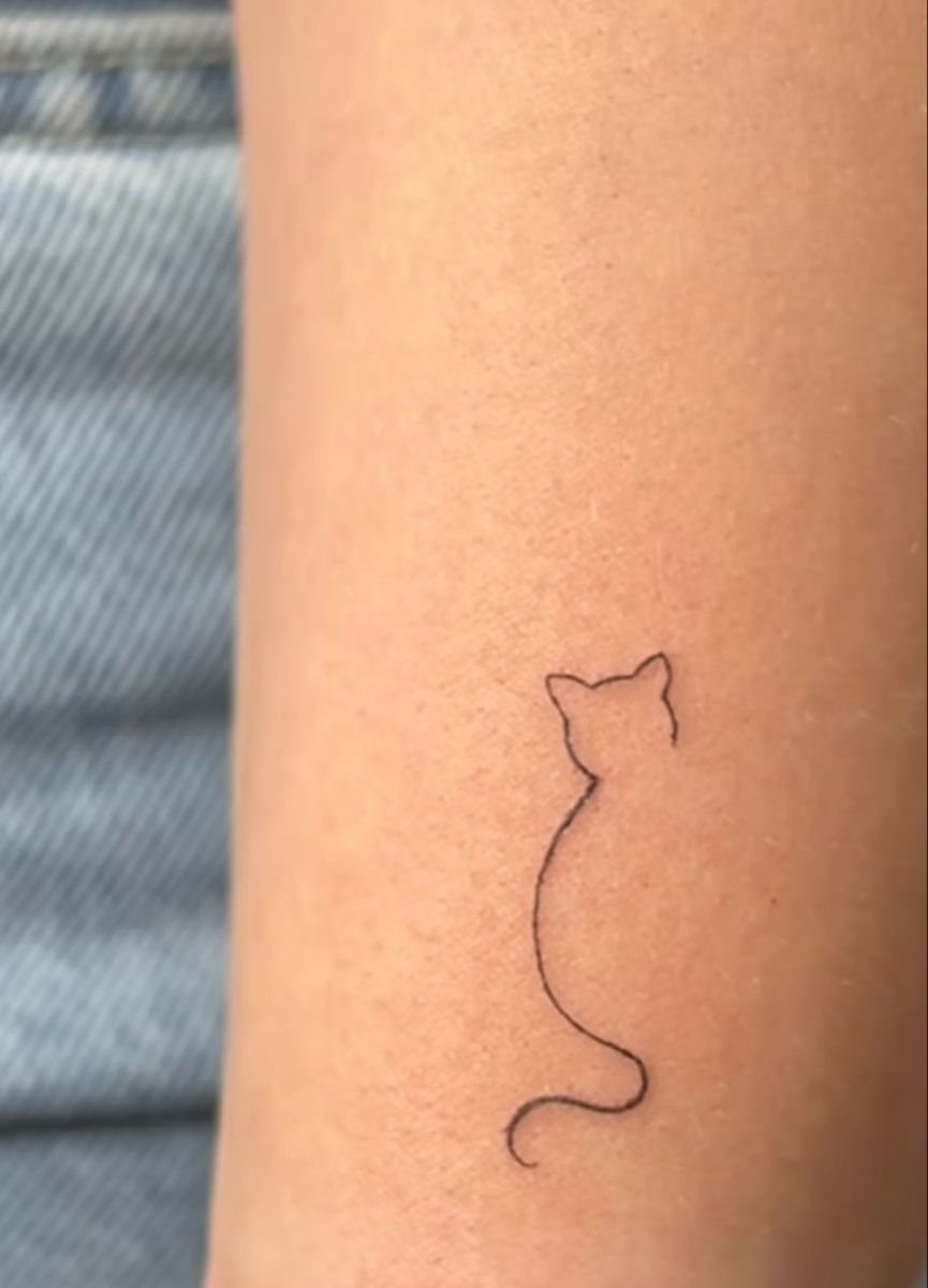 A minimalist fine line tattoo of a cat silhouette on a person's arm.