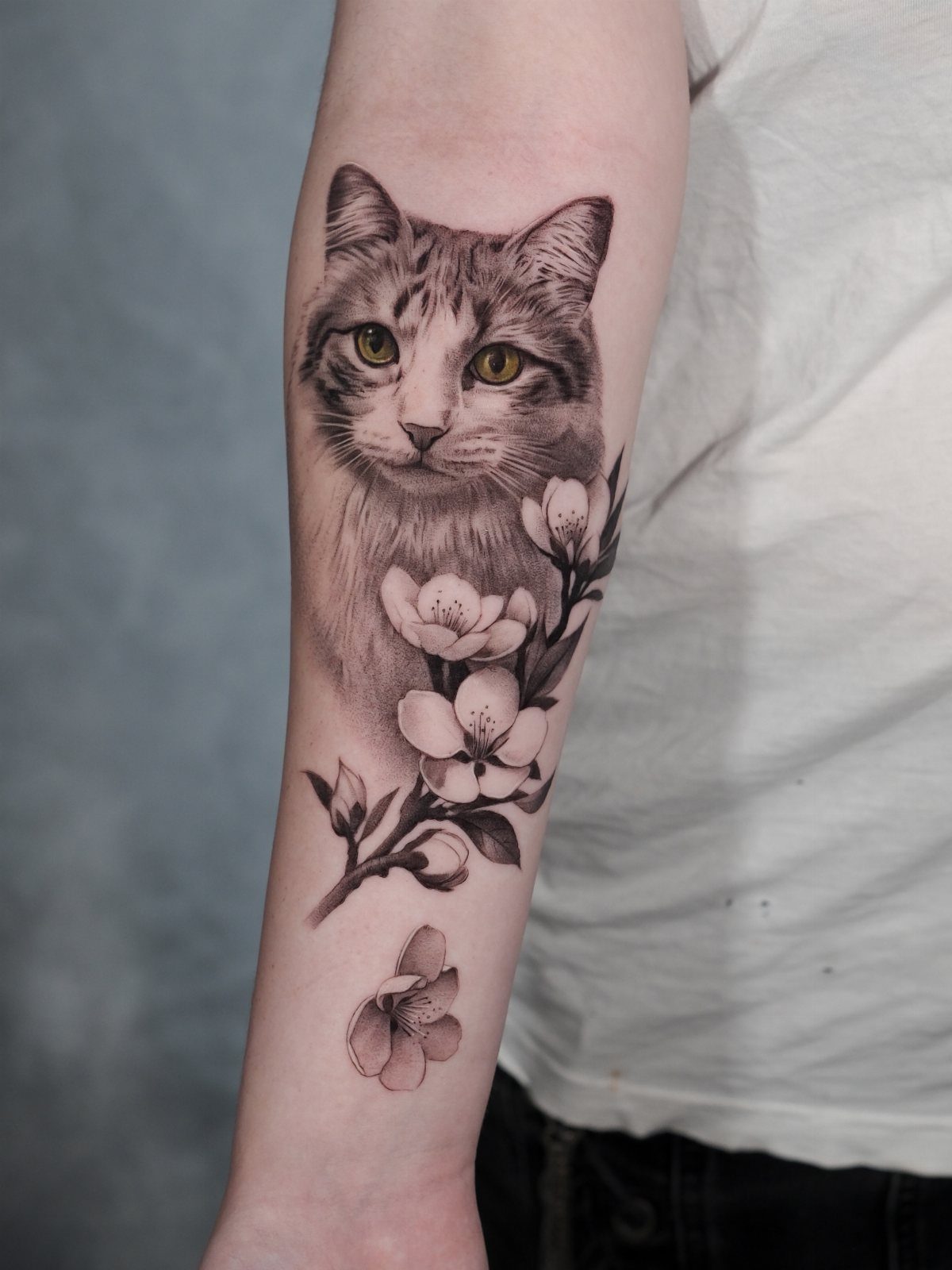 A realistic cat face tattoo with flowers on a person's forearm.