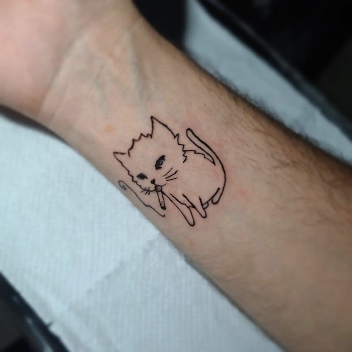 A small black ink fine line cat tattoo on a person's wrist.