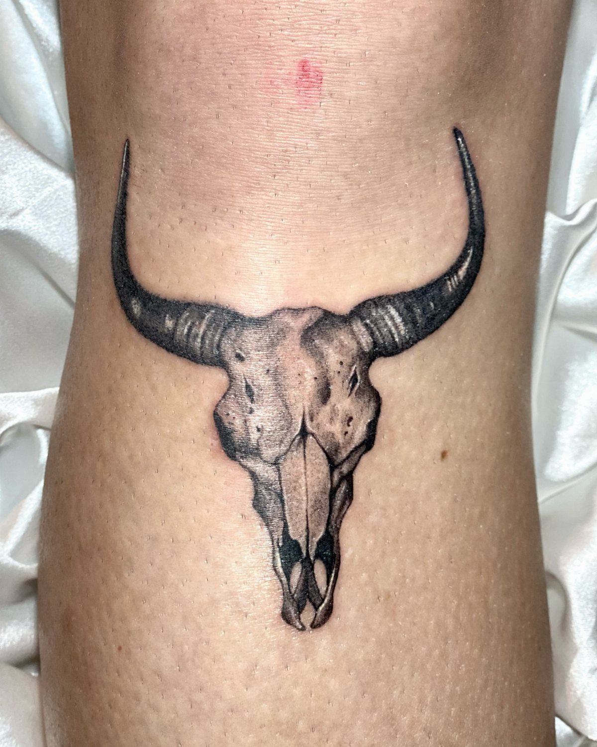 A black and grey realism tattoo of a cow skull on human skin.