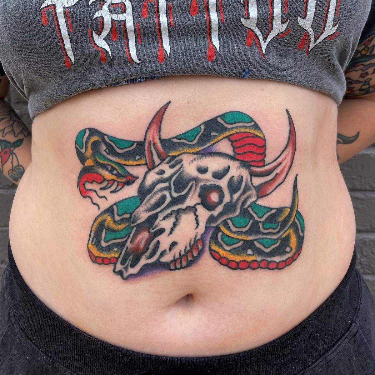 A colorful tattoo of a cow skull entwined with a patterned snake on a person's stomach.