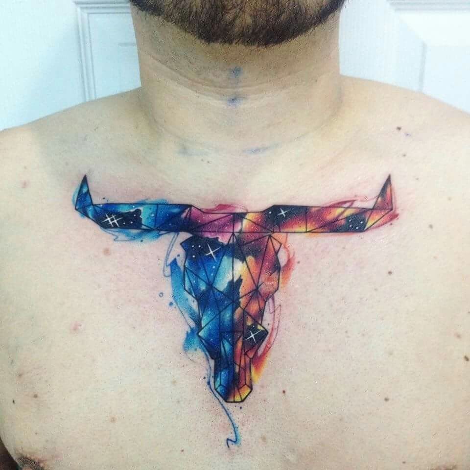 A colorful geometric cow skull tattoo with watercolor splashes on a person's chest.
