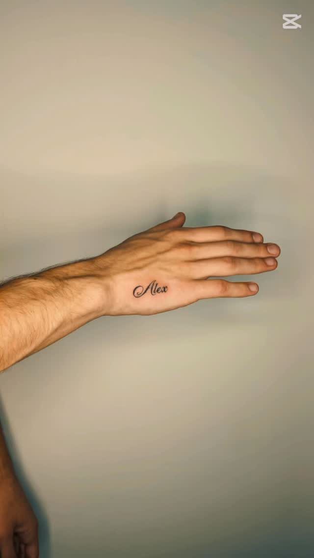 A hand with a small cursive tattoo of the name Alex on the side.