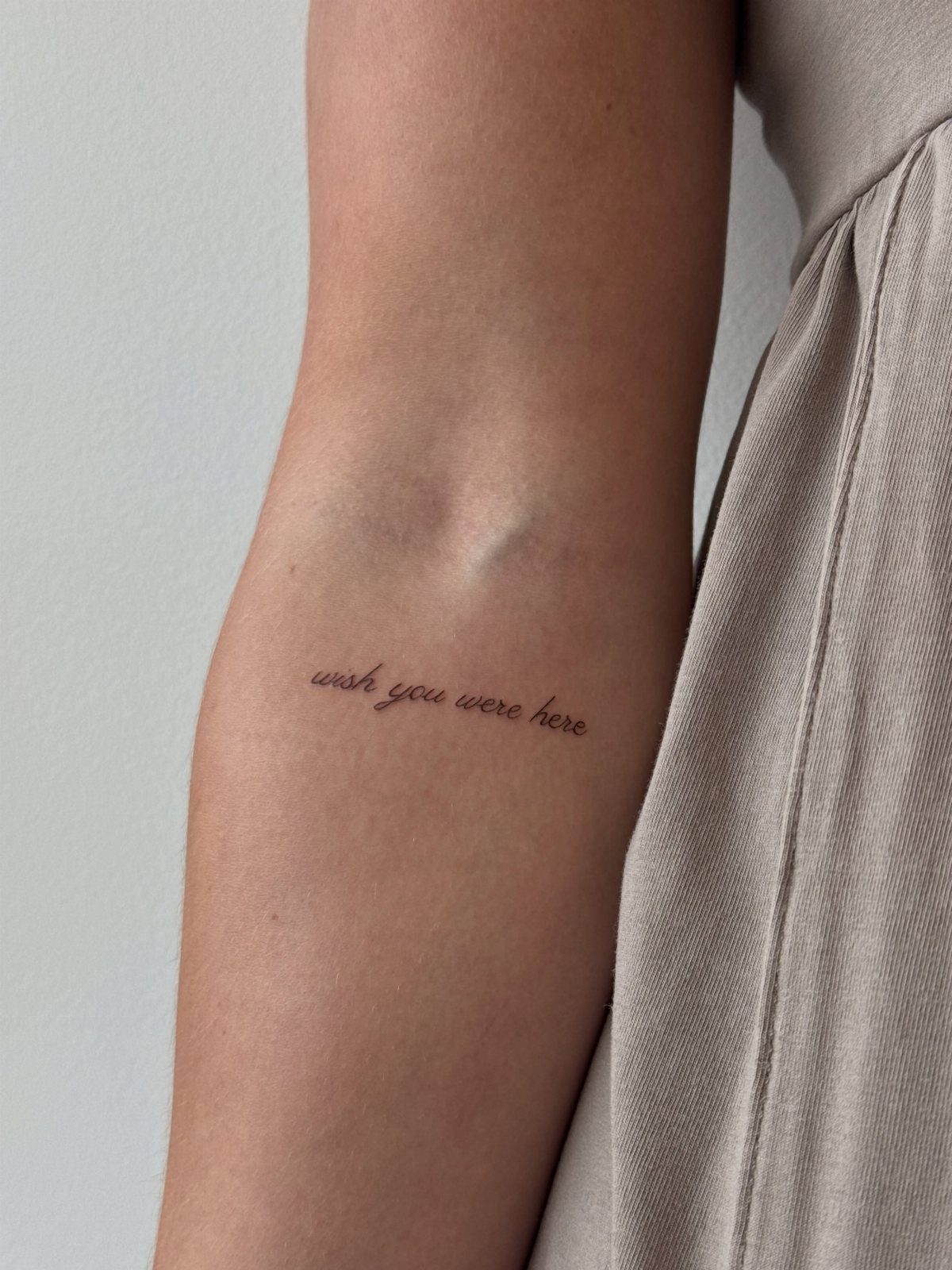 A small cursive tattoo on a person's arm reading wish you were here.