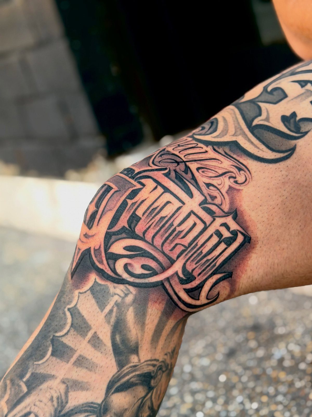 A large black and grey tattoo with stylized lettering on a person's arm.