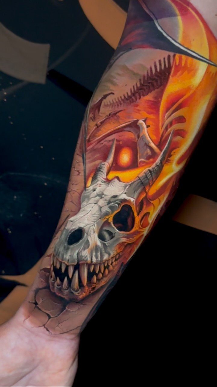 A colorful dragon skull tattoo with fiery orange and red tones on a person's forearm.