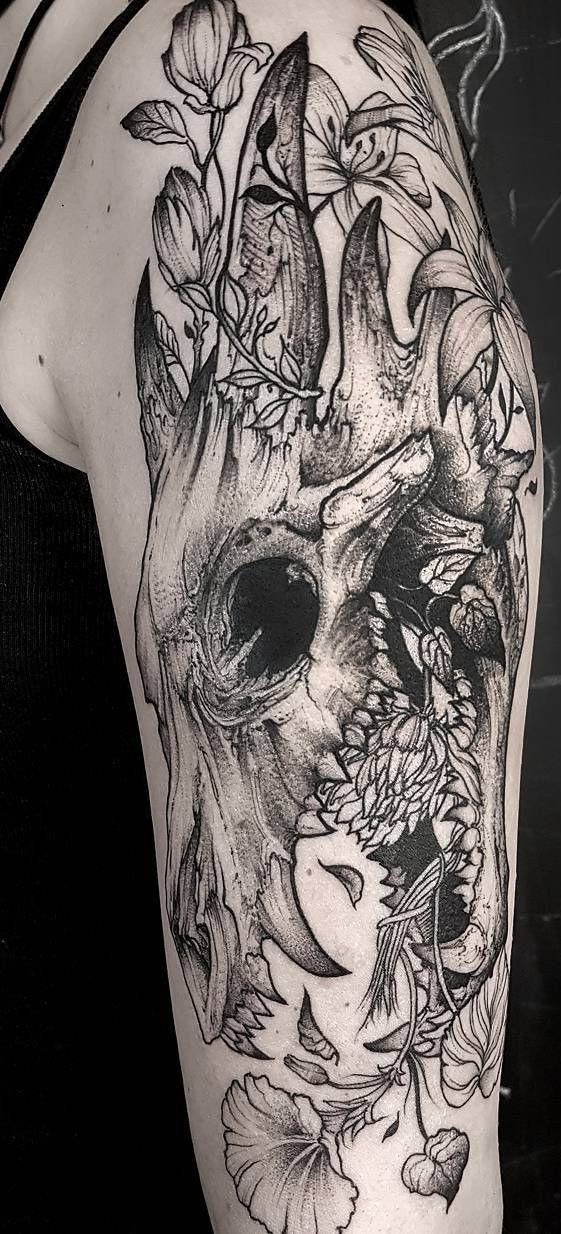 A detailed black and grey dragon skull tattoo surrounded by delicate floral patterns on a person's arm.
