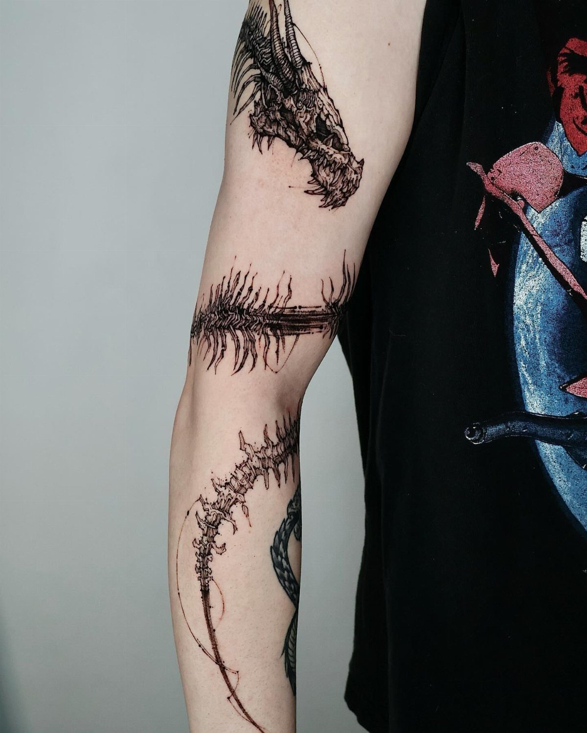 A black ink dragon skull and skeletal spine tattoo on a person's arm.