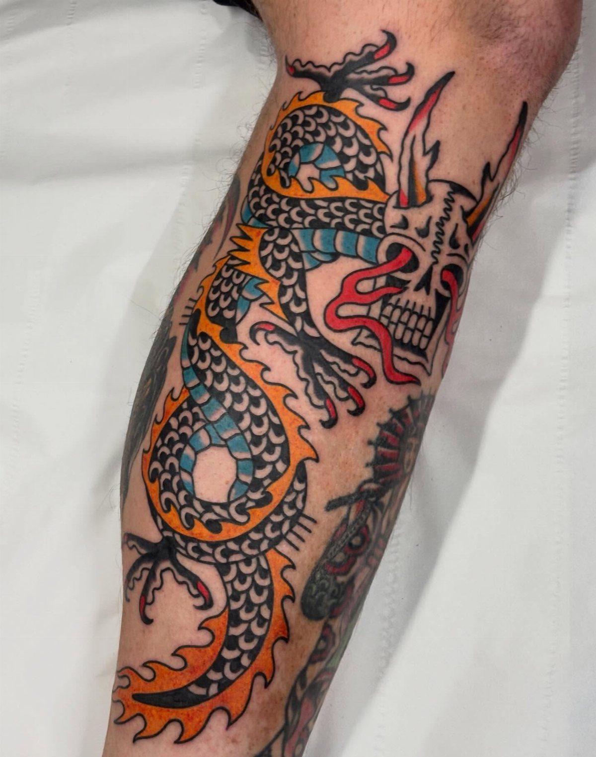 A colorful serpentine dragon skull tattoo with orange and blue scales on a person's leg.