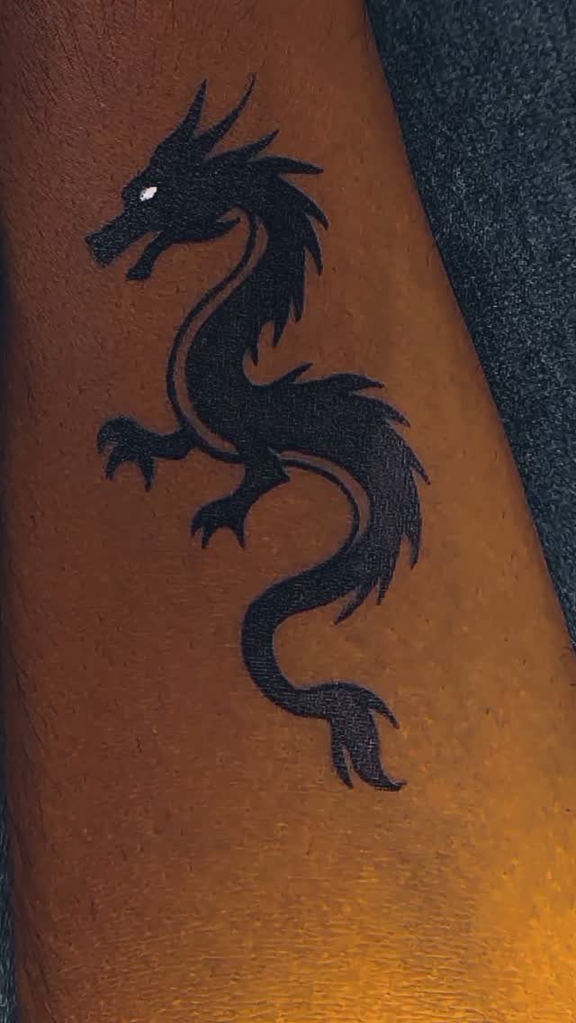 12 Easy Tattoo Drawings For Beginners, From Hearts to Tribal Flash 10 A black ink dragon tattoo with a serpentine body on human skin.