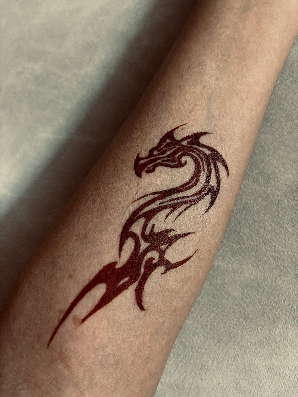 12 Easy Tattoo Drawings For Beginners, From Hearts to Tribal Flash 3 A dark red tribal dragon tattoo on a person's forearm.