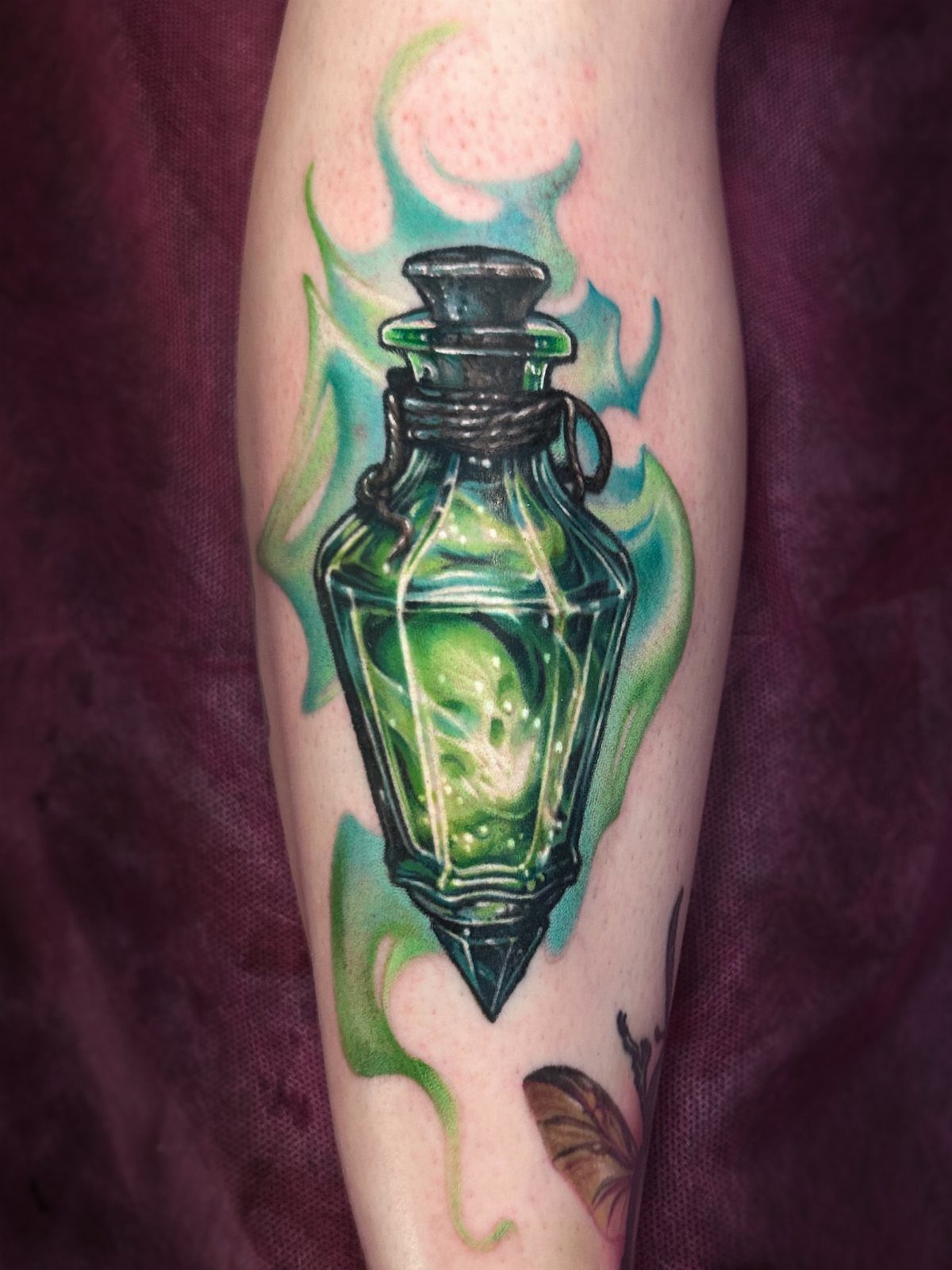 A vibrant green potion bottle tattoo with glowing magical swirls on a person's leg.