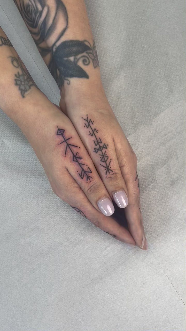 Two hands displaying black ink tattoos of geometric, rune-like symbols against a white background.