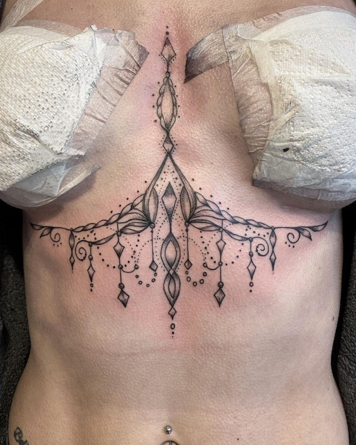 Ornamental geometric tattoo with fine lines and dotwork on a person's sternum and ribs.