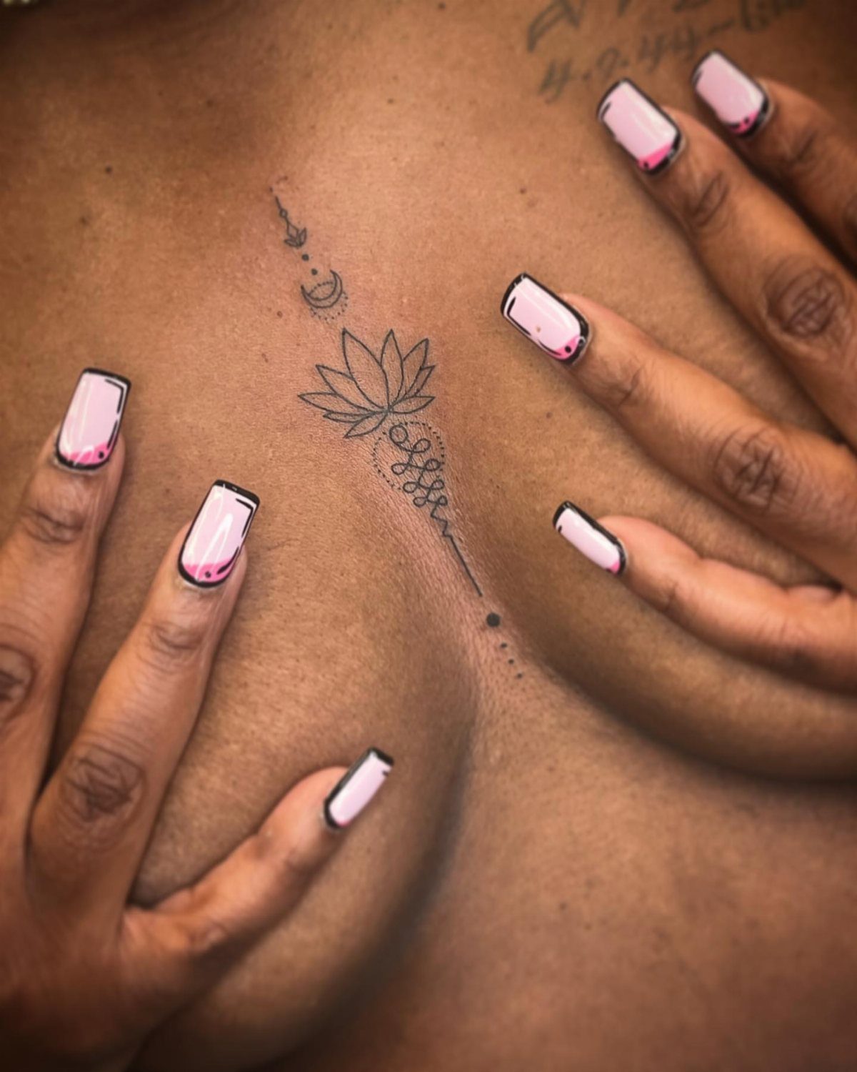 A fine line lotus flower tattoo with ornamental details on a person's sternum.