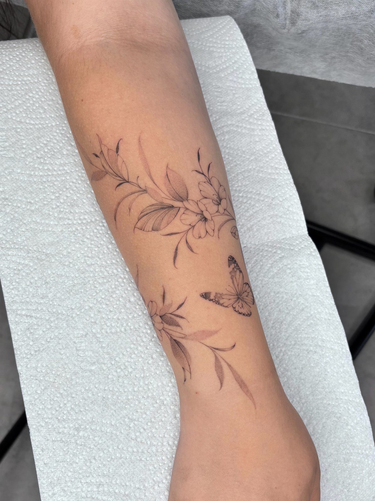 5 Fine Line Flower Vine Tattoo Ideas for Placement and Flow 4 A forearm tattoo featuring fine line floral vines and a small butterfly design.