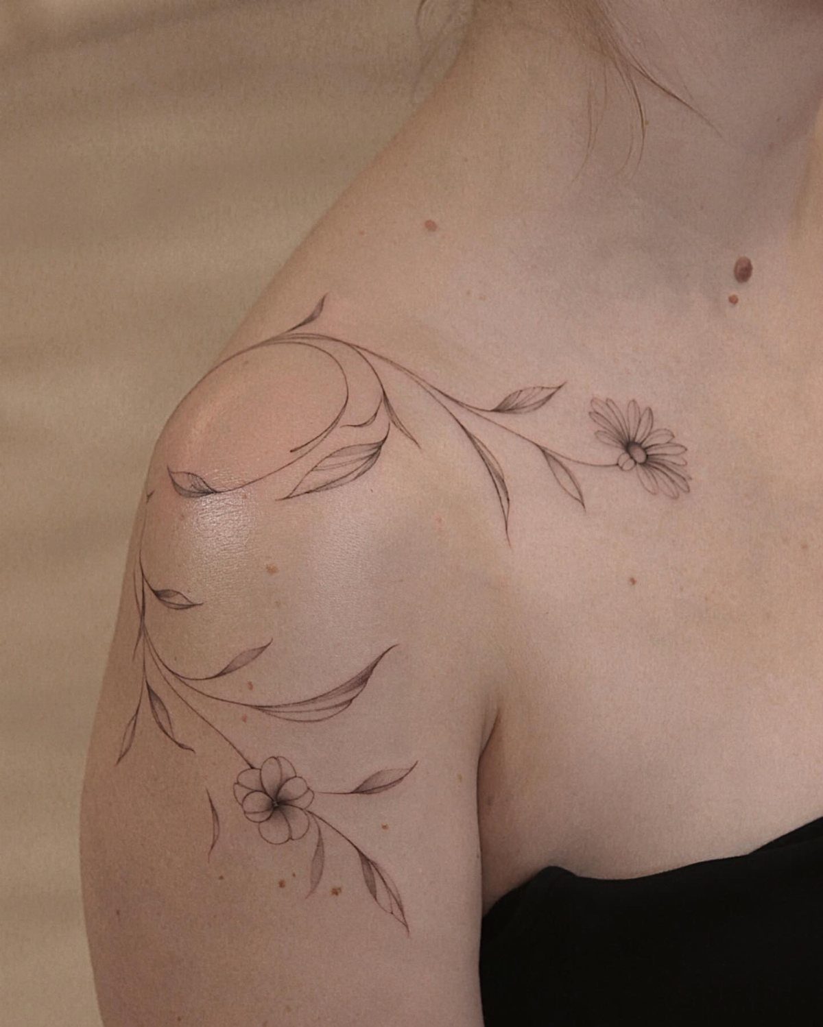 5 Fine Line Flower Vine Tattoo Ideas for Placement and Flow 5 A fine line flower vine tattoo with small blossoms on a person's shoulder and collarbone.