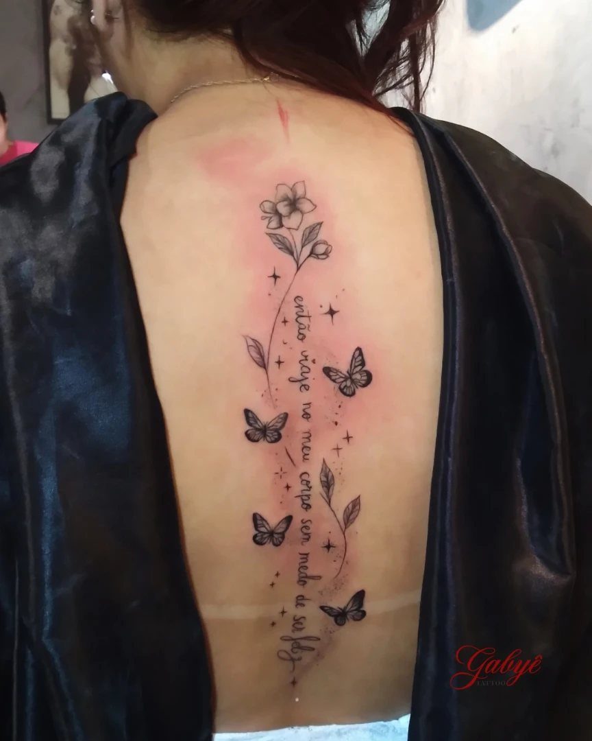 5 Fine Line Flower Vine Tattoo Ideas for Placement and Flow 3 A vertical fine line tattoo with flowers, butterflies, and text on a person's back.