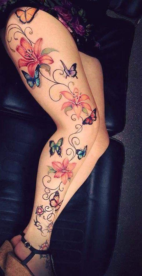 A person's leg featuring a large tattoo of pink lilies, swirling vines, and colorful butterflies.