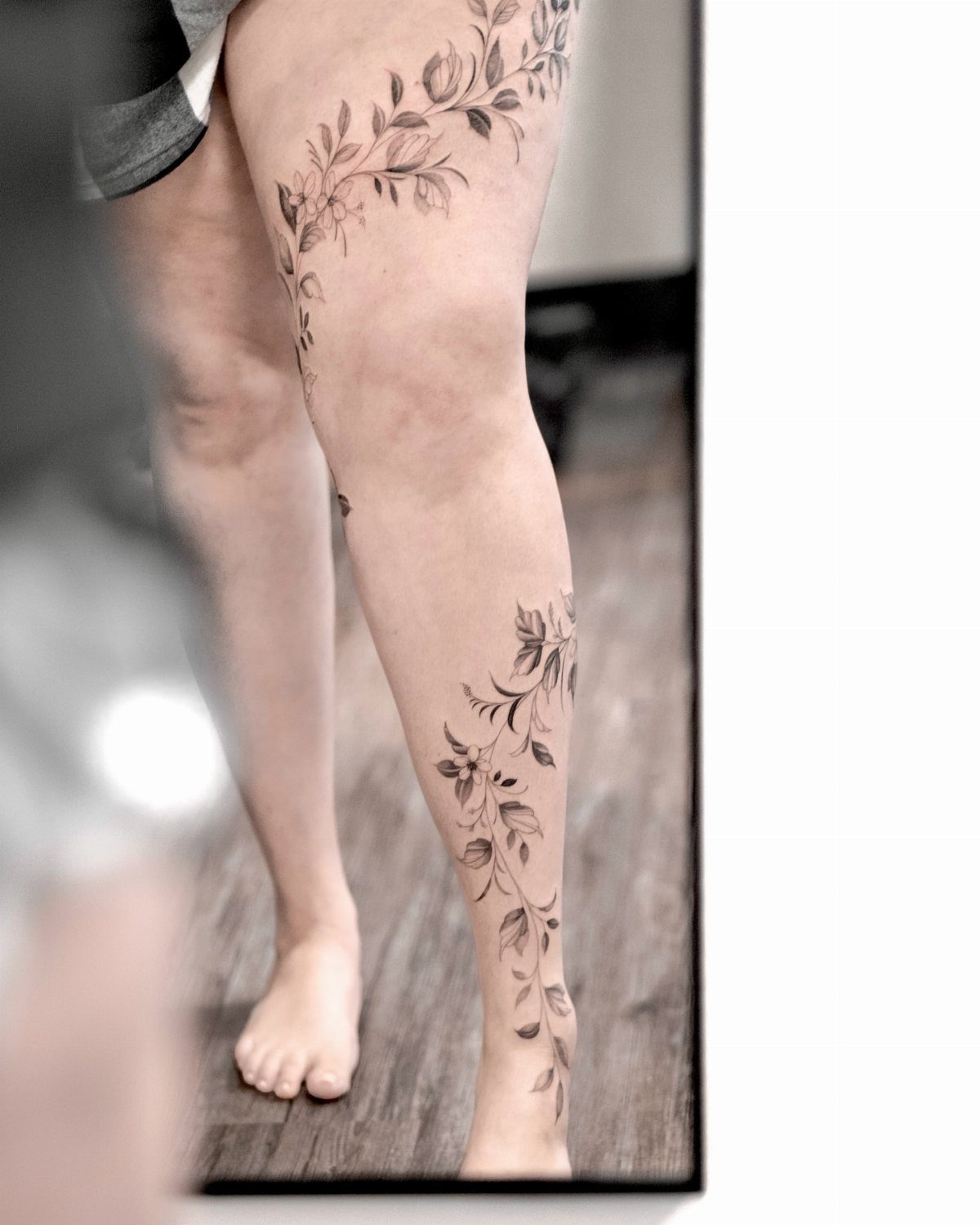 Botanical tattoos of leaves and flowers trailing down a person's leg and calf.
