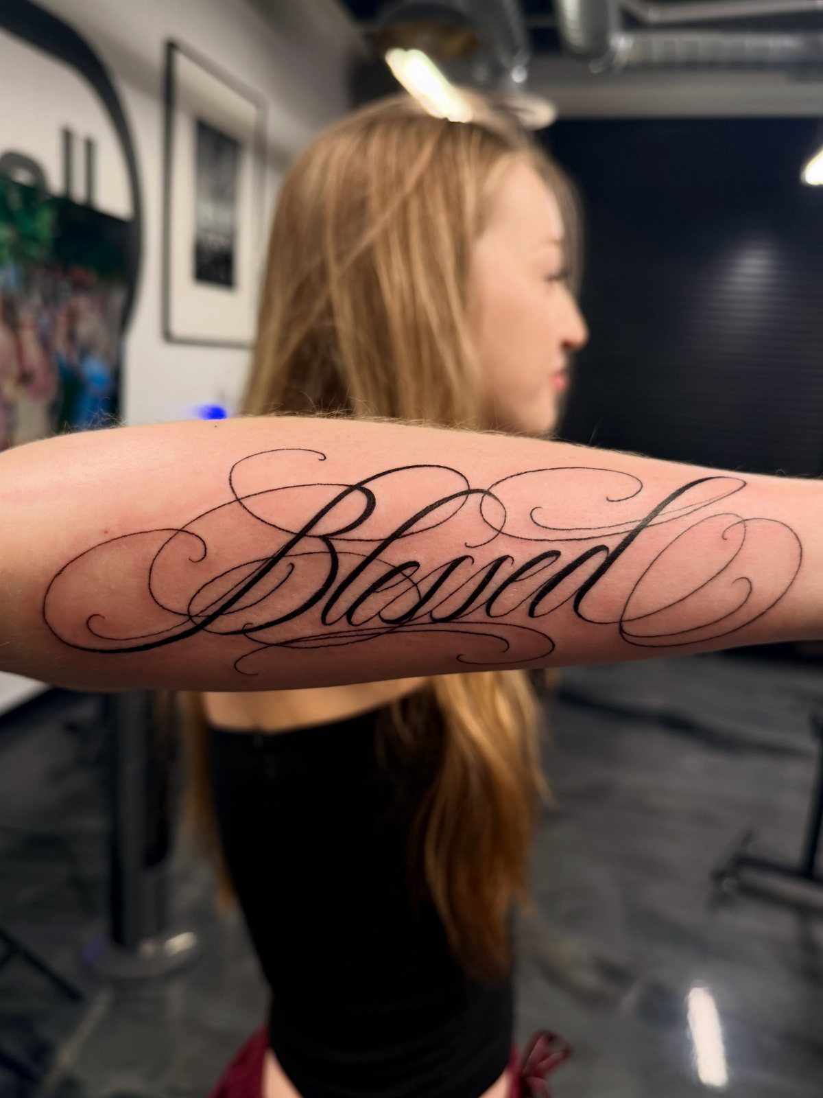 8 Forearm Cursive Tattoo Ideas for Script That Means Something 1 A forearm tattoo of the word 'Blessed' in elegant, decorative black cursive script.