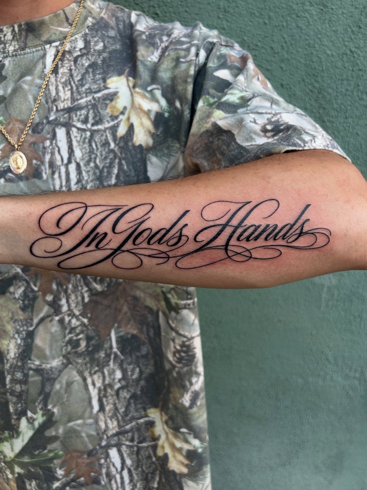8 Forearm Cursive Tattoo Ideas for Script That Means Something 7 A person's forearm displaying a large black cursive tattoo that says In Gods Hands.