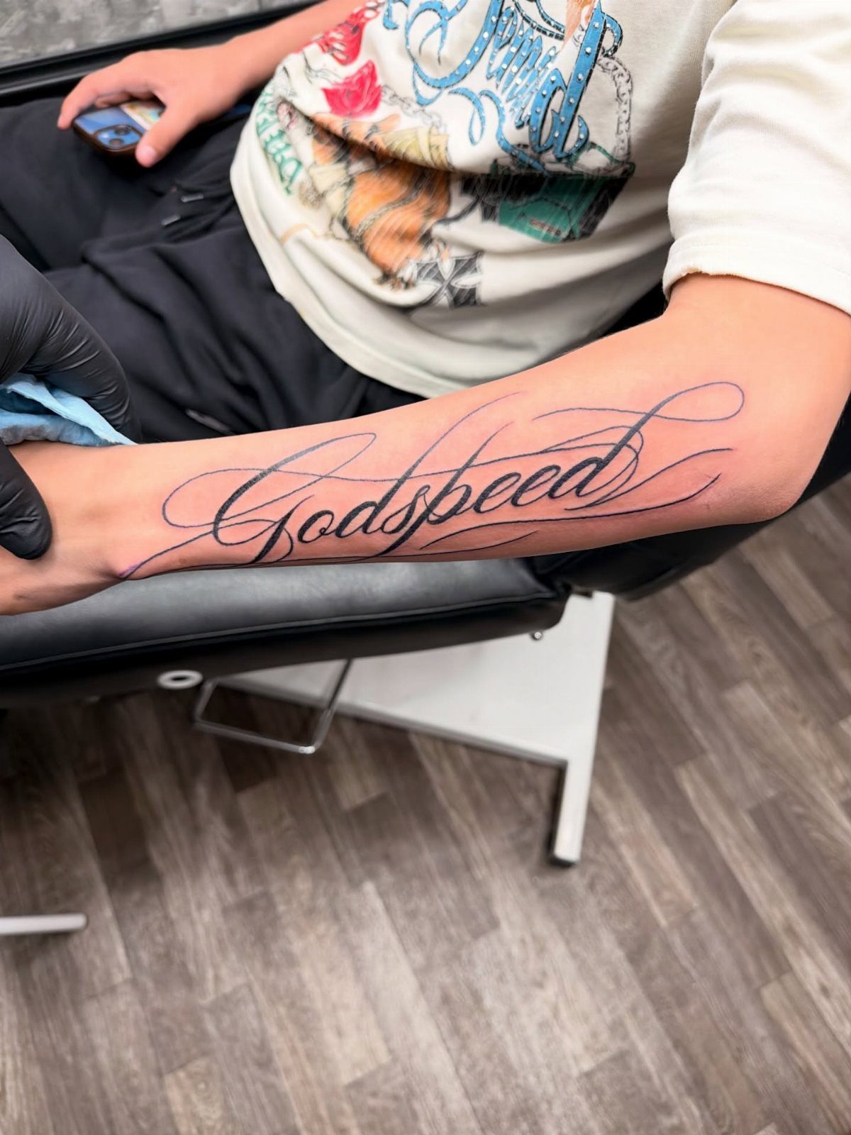 8 Forearm Cursive Tattoo Ideas for Script That Means Something 2 A person's forearm displaying a large black cursive tattoo of the word Godspeed.