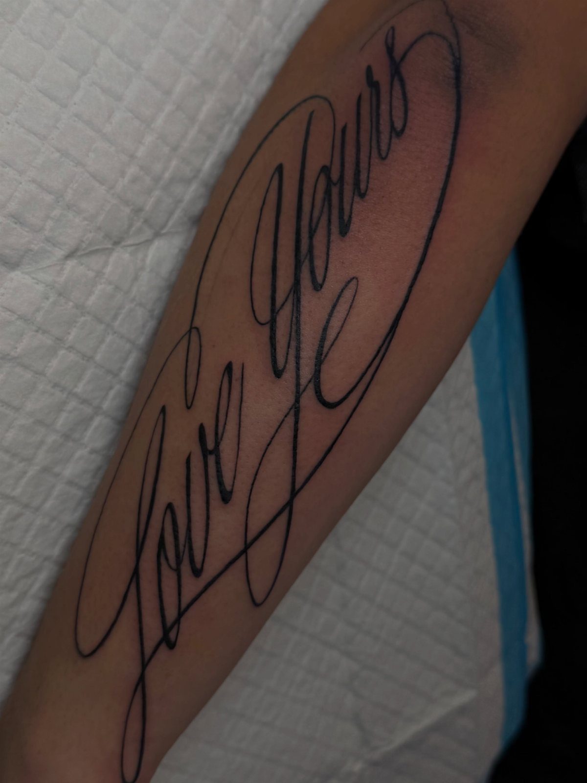 8 Forearm Cursive Tattoo Ideas for Script That Means Something 5 A forearm featuring a large black ink cursive tattoo that reads Love Yours.