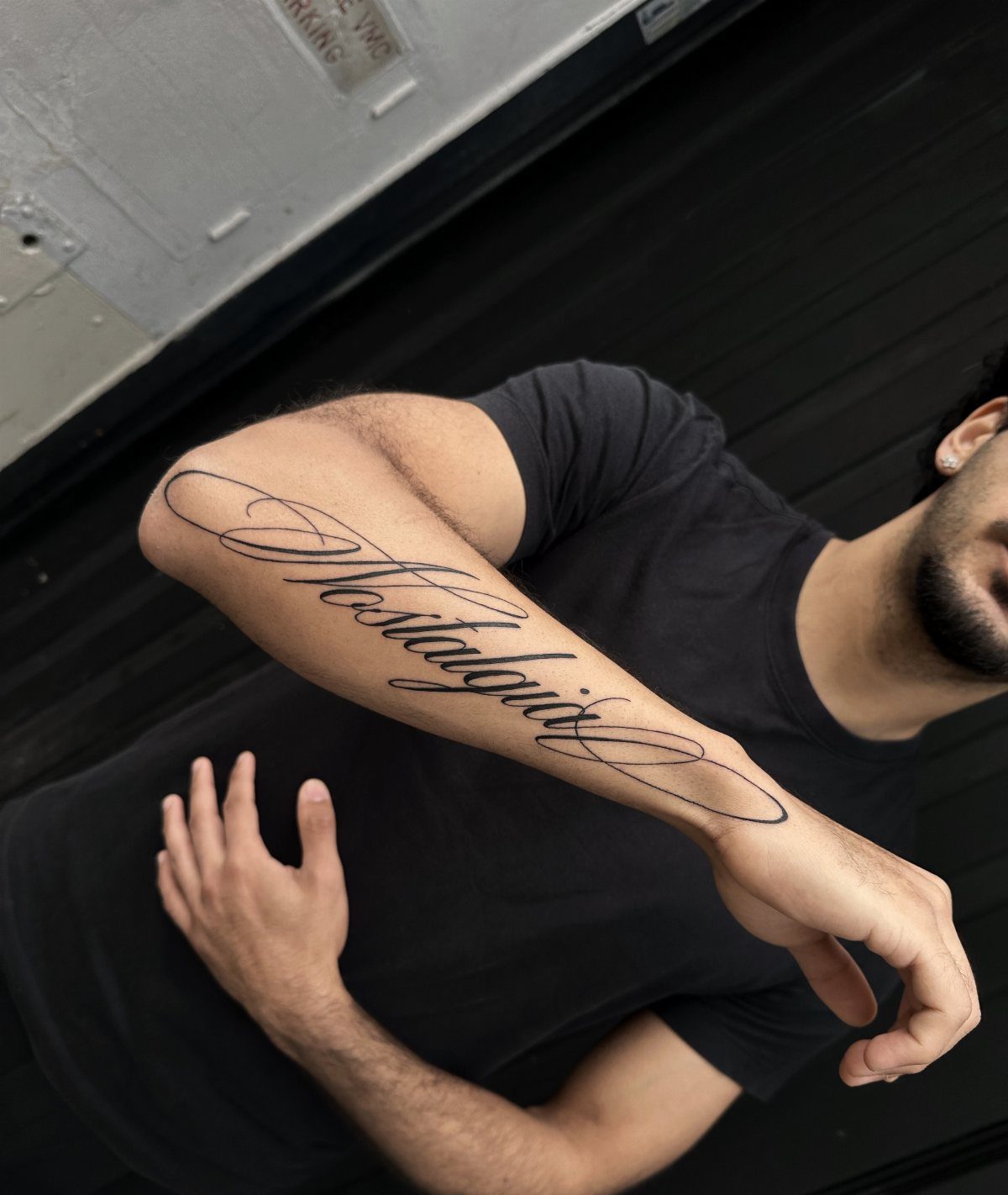 8 Forearm Cursive Tattoo Ideas for Script That Means Something 3 A man's forearm displaying a large black cursive tattoo of the word Nostalgia.