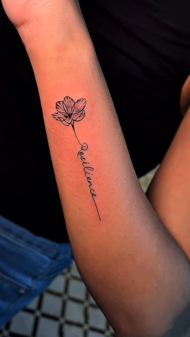 8 Forearm Cursive Tattoo Ideas for Script That Means Something 4 A forearm tattoo of a small flower with a stem forming the word Resilience in cursive.