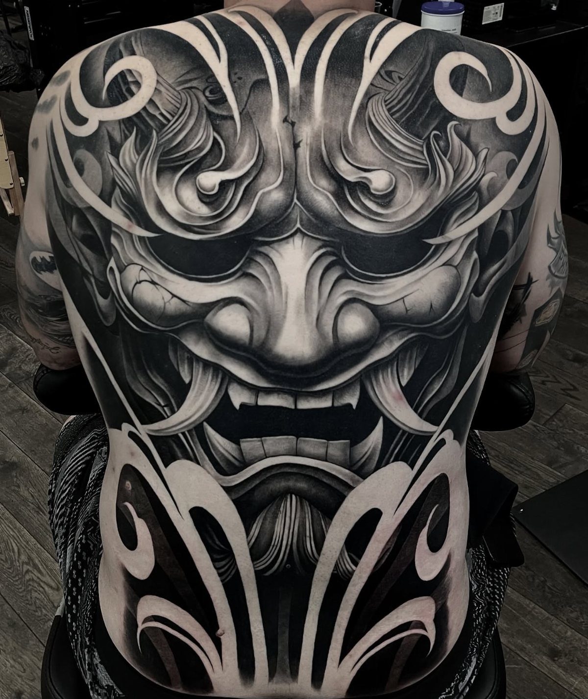 A large black and grey Japanese demon mask tattoo covering a person's entire back.