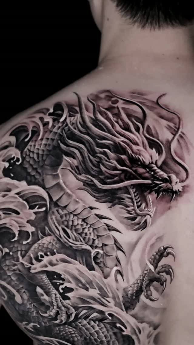 A large black and grey dragon tattoo winding across a person's upper back and shoulder.